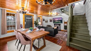 Een eethoek met een houten tafel en stoelen, een bank en een open haard. Er bevindt zich een trap aan de rechterkant.