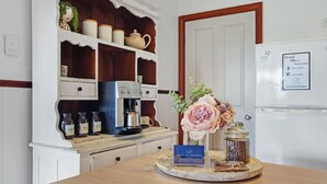 Una cocina con una cafetera, estantes con frascos, un florero con flores y un cartel en la encimera.