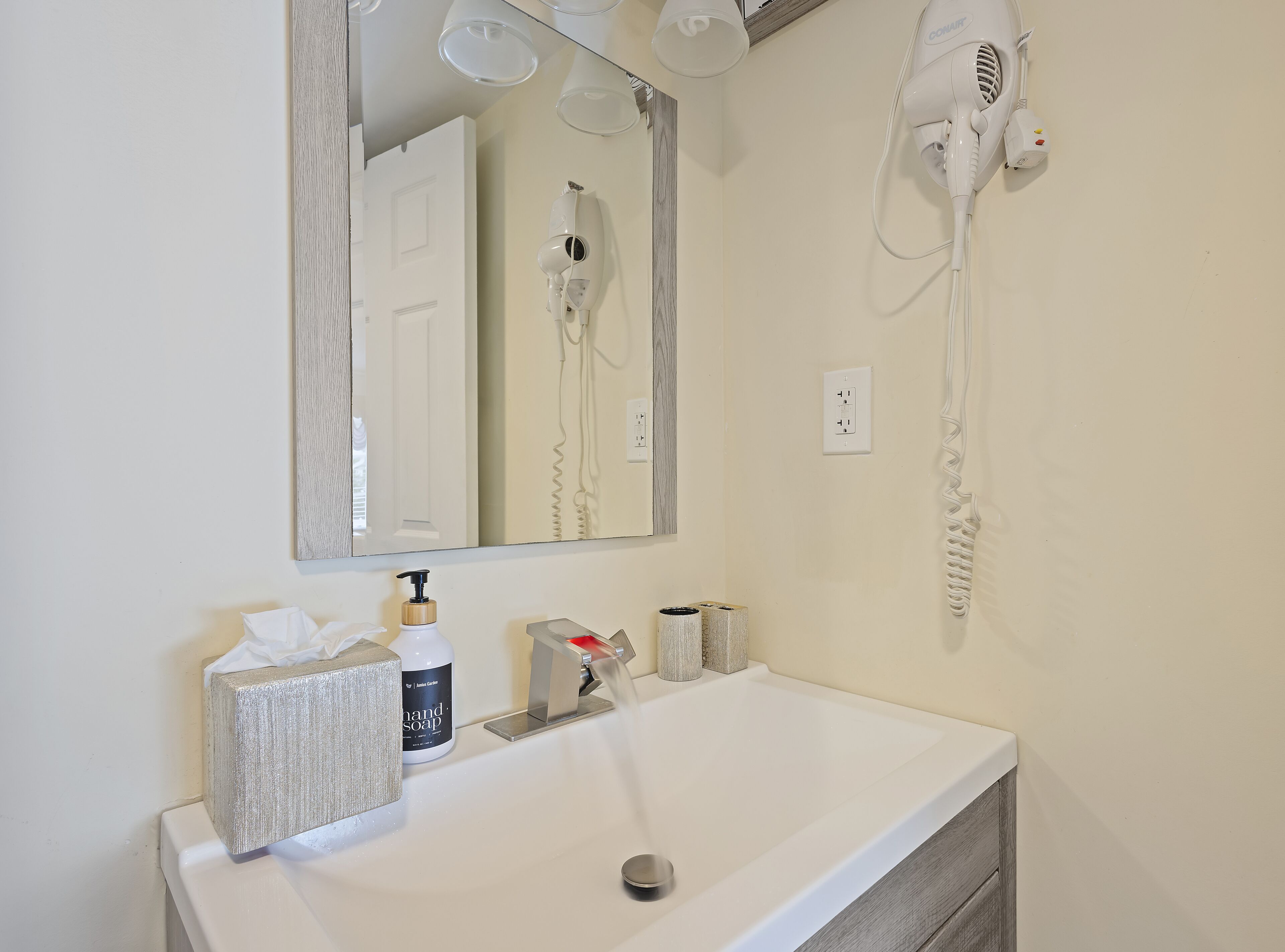 A bathroom with a white sink, a mirror, a hairdryer, and a bottle of hand soap.