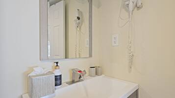 A bathroom with a white sink, a mirror, a hairdryer, and a bottle of hand soap.