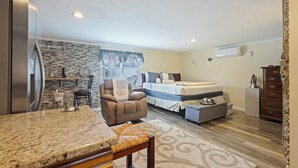A compact hotel room with a kitchenette, a bed, a seating area with a chair, and a small table. - C & N Lodging, Bluffton, SC (Bluffton)