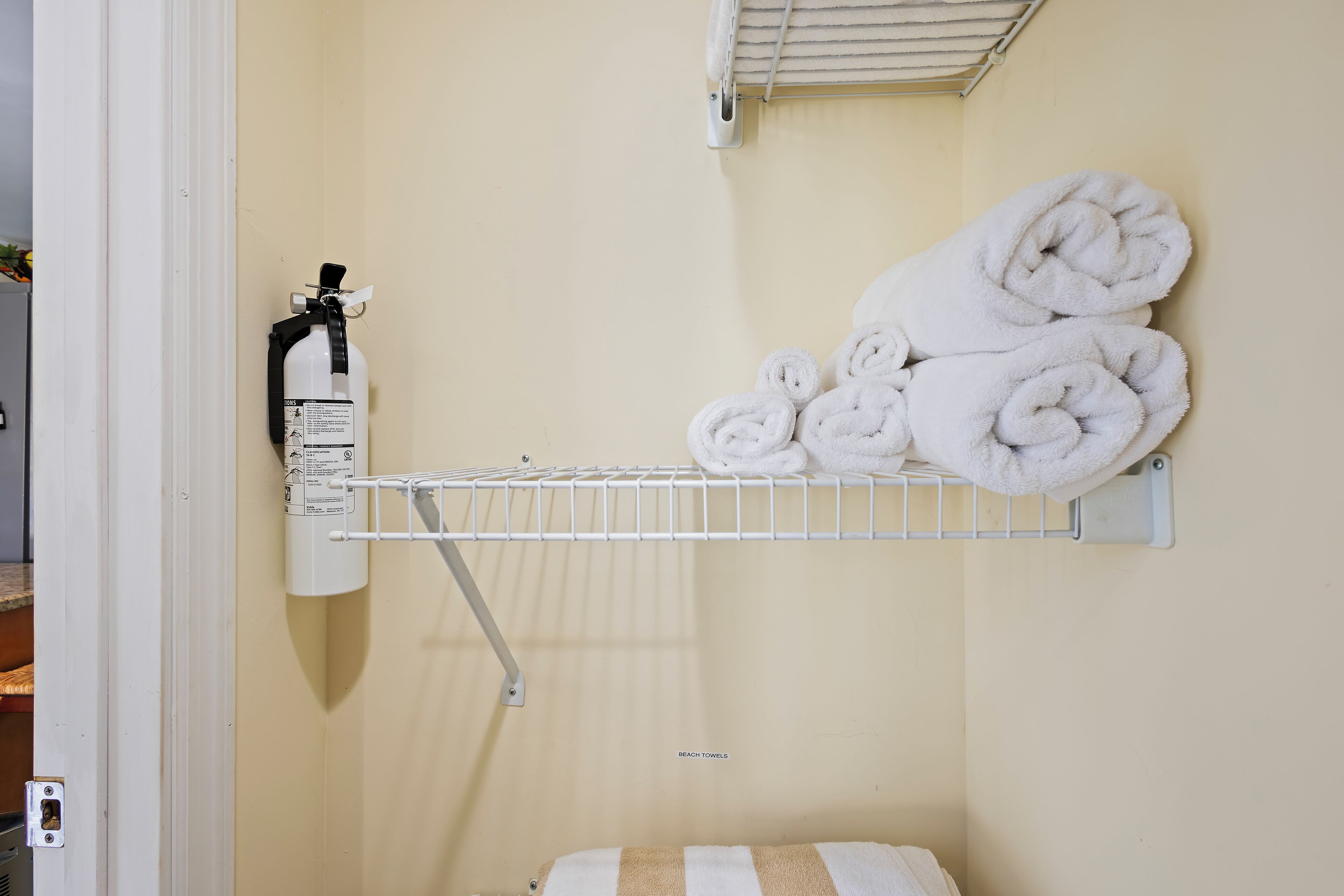 A bathroom with a towel rack holding rolled towels and a fire extinguisher mounted on the wall.