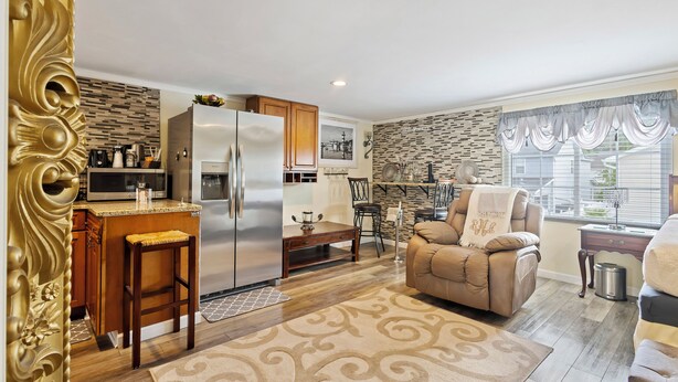 A modern kitchen with a built-in refrigerator, microwave, and coffee maker. There is a dining area with a wooden table and chairs, and a living room with a sofa and a window with curtains. - C & N Lodging, Bluffton, SC (Bluffton)