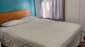 Un dormitorio con cama, cabecera, ventana con cortinas y detector de humo instalado en la pared.