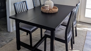 A dining area with a dark wooden table, four chairs, a woven basket with a candle, and a vase with greenery. - Scottsdale Kierland Mayo Clinic Desert Ridge (Phoenix)
