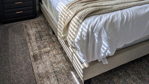 A neatly made bed with a white comforter and a beige throw blanket, a bedside table with a lamp, and a painting on the wall. - Scottsdale Kierland Mayo Clinic Desert Ridge (Phoenix)