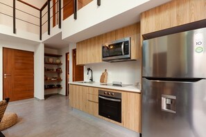 A modern kitchen with wooden cabinets, a stainless steel refrigerator, a microwave, and an oven.