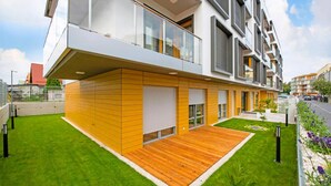A modern multi-story residential building with a flat roof, large windows, and a wooden deck.