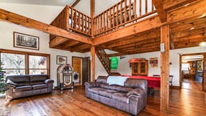 Ein geräumiges Wohnzimmer mit Holzböden und hoher Decke, ausgestattet mit zwei Ledersofas, einer Holztreppe und einem sichtbaren Schild der Landespolizei.