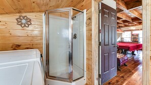 Ein Holzblockhaus-Interieur mit einer Glaskabine für eine Dusche, einer Tür zu einem Essbereich mit roter Tischdecke und Holzböden.