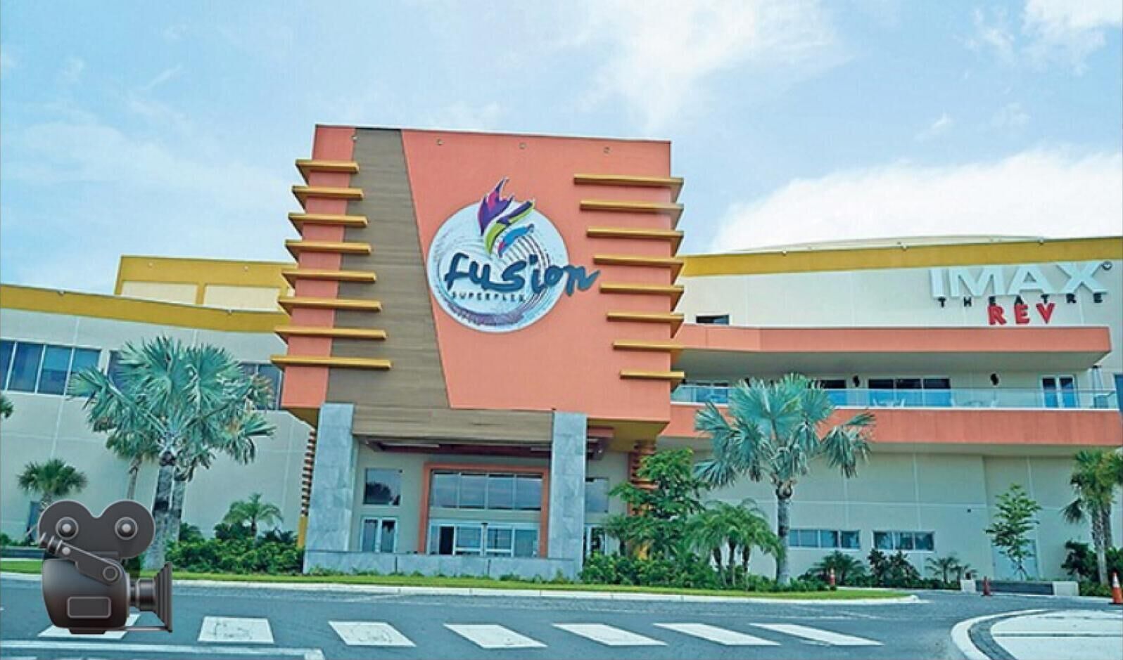 A building with a prominent 'FUSION' sign, a 'IMAX' theater, and a palm tree-lined entrance.