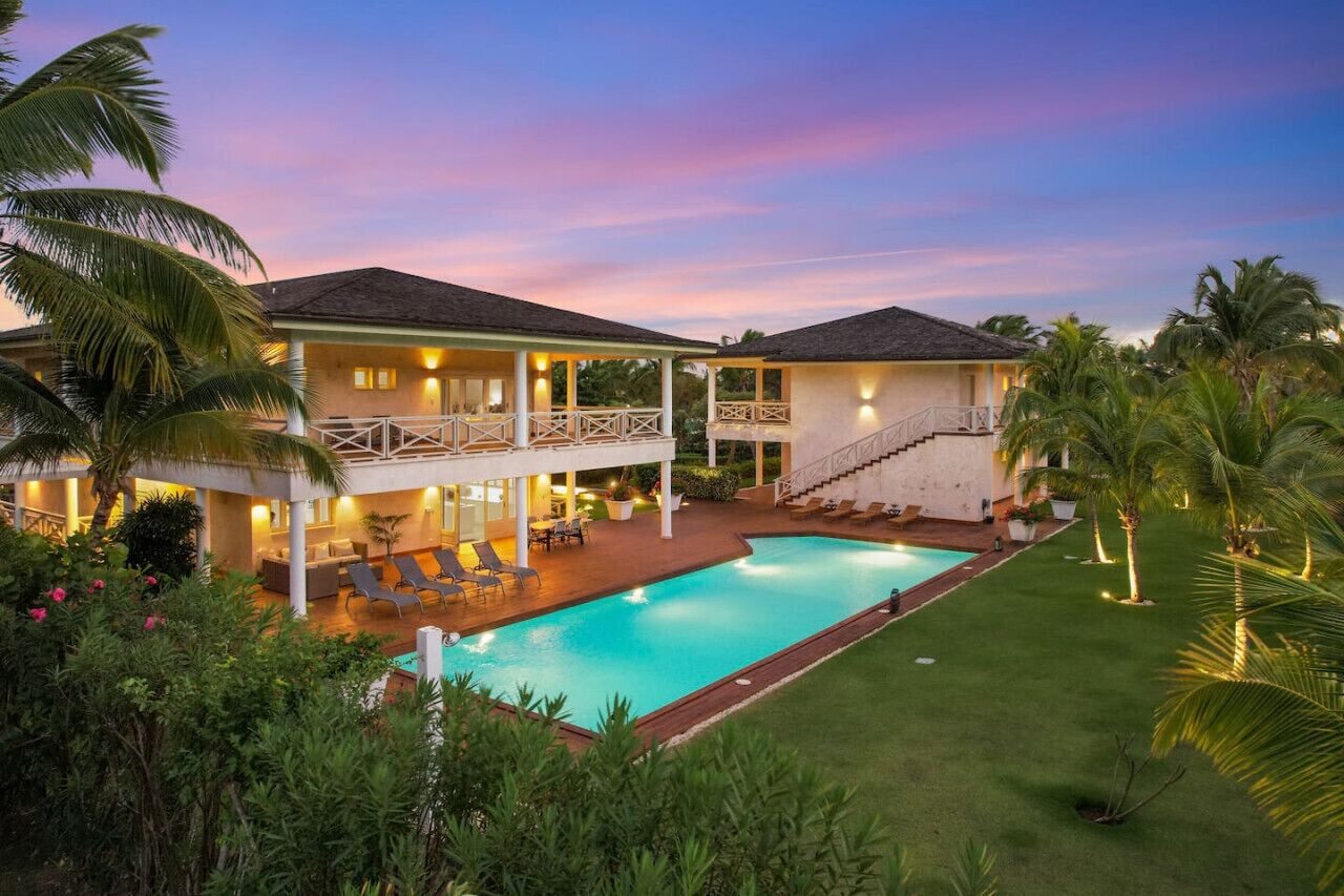 A two-story house with a swimming pool, outdoor seating, and a well-maintained lawn.