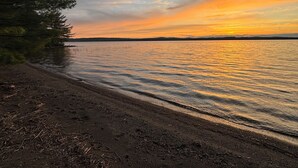 Een strand met uitzicht op een zonsondergang, rustig water en een bebost gebied.