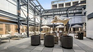 Un área de estar al aire libre con muebles modernos, grandes macetas y un edificio de vidrio al fondo.