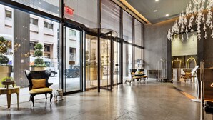 Un lobby moderno de hotel con grandes puertas de vidrio, un mostrador de recepción y un candelabro.
