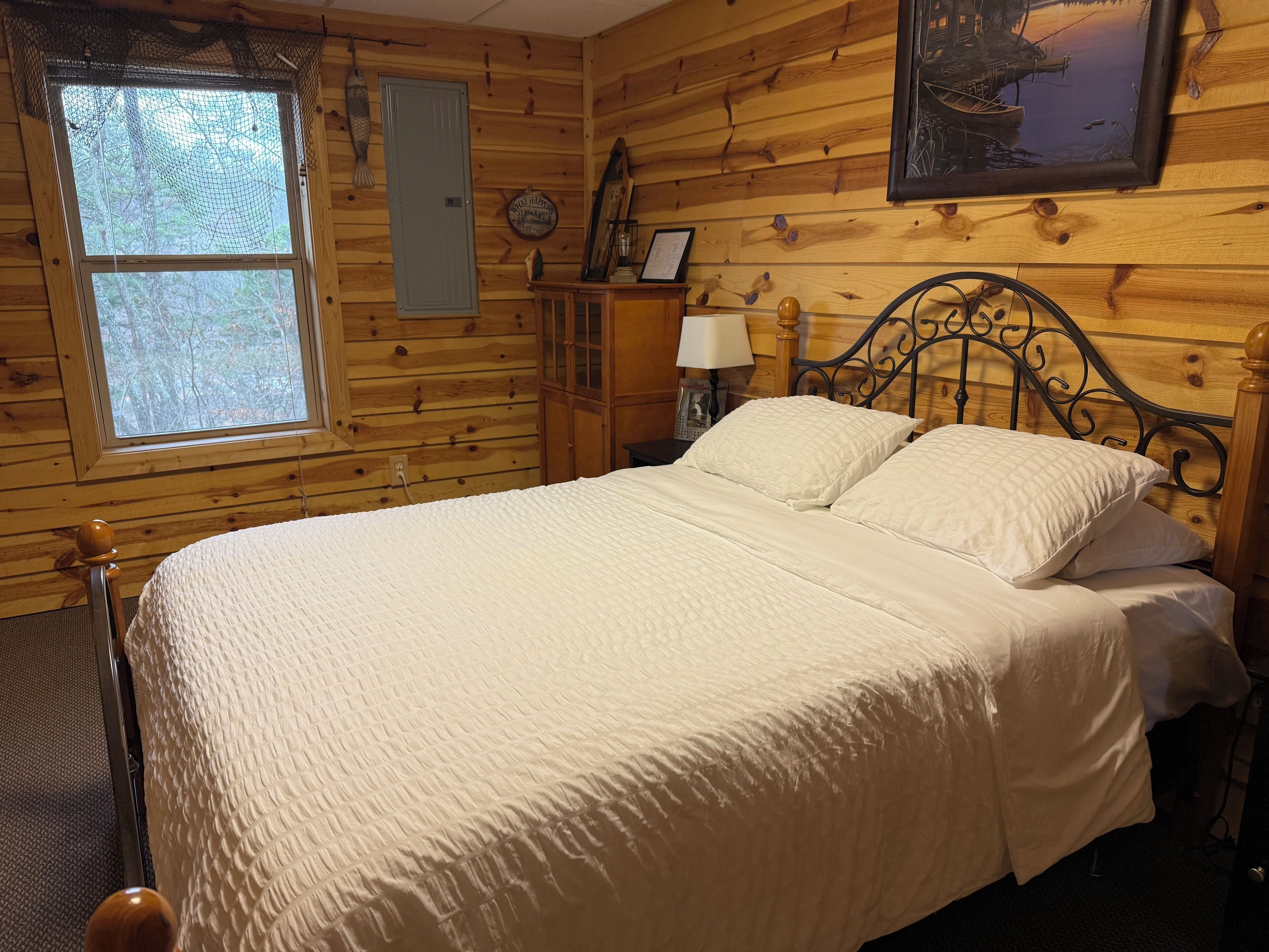 Una habitación de cabaña de madera con una cama, una ventana, una puerta y un cuadro en la pared.
