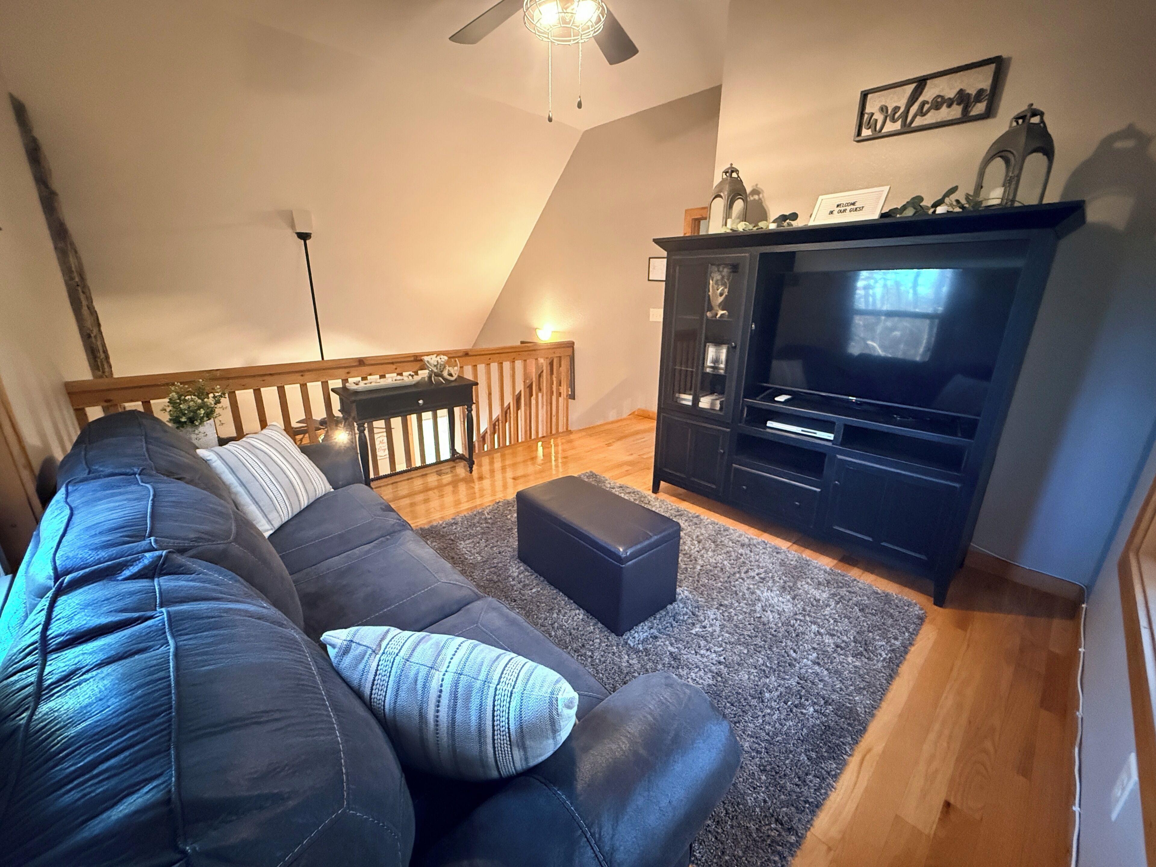 A living room with a dark-colored sofa, a flat-screen TV, and a wooden staircase.