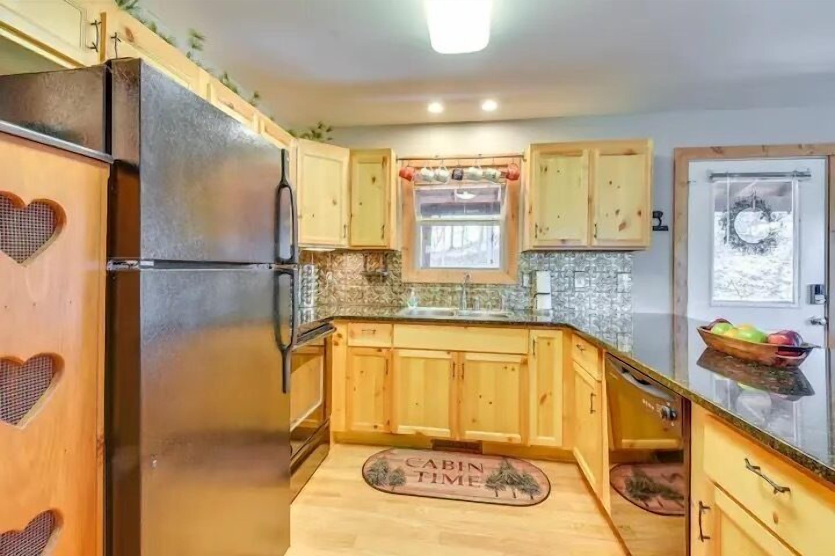 A compact kitchen with wooden cabinets, a stainless steel refrigerator, and a small window.