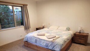 A bedroom with a wooden bed, two bedside tables, a window with curtains, and a view of a backyard.