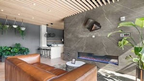 A modern living room with a leather sofa, a fireplace, and a kitchen in the background. - 3BR/2BA Lux Condo | Pool |Walk to Broadway (0.8mi) (Nashville)