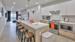 A modern kitchen with a central island, bar stools, a sink, and a stove. - 3BR/2BA Lux Condo | Pool |Walk to Broadway (0.8mi) (Nashville)