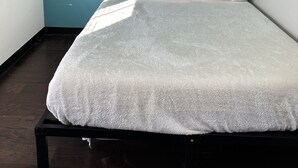 Una cama individual en una habitación con paredes verde azulado y suelo oscuro.