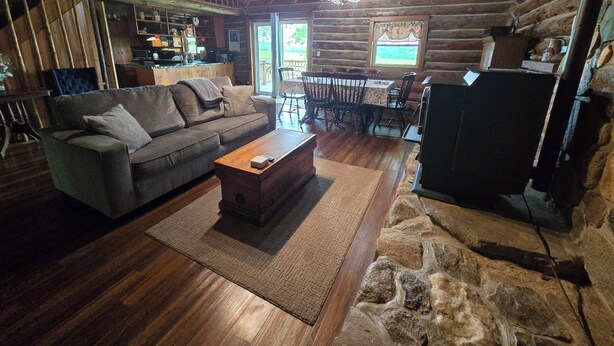 L’intérieur d’une cabane en rondins, avec un canapé, une table basse, une table à manger, des chaises et une cheminée en pierre.