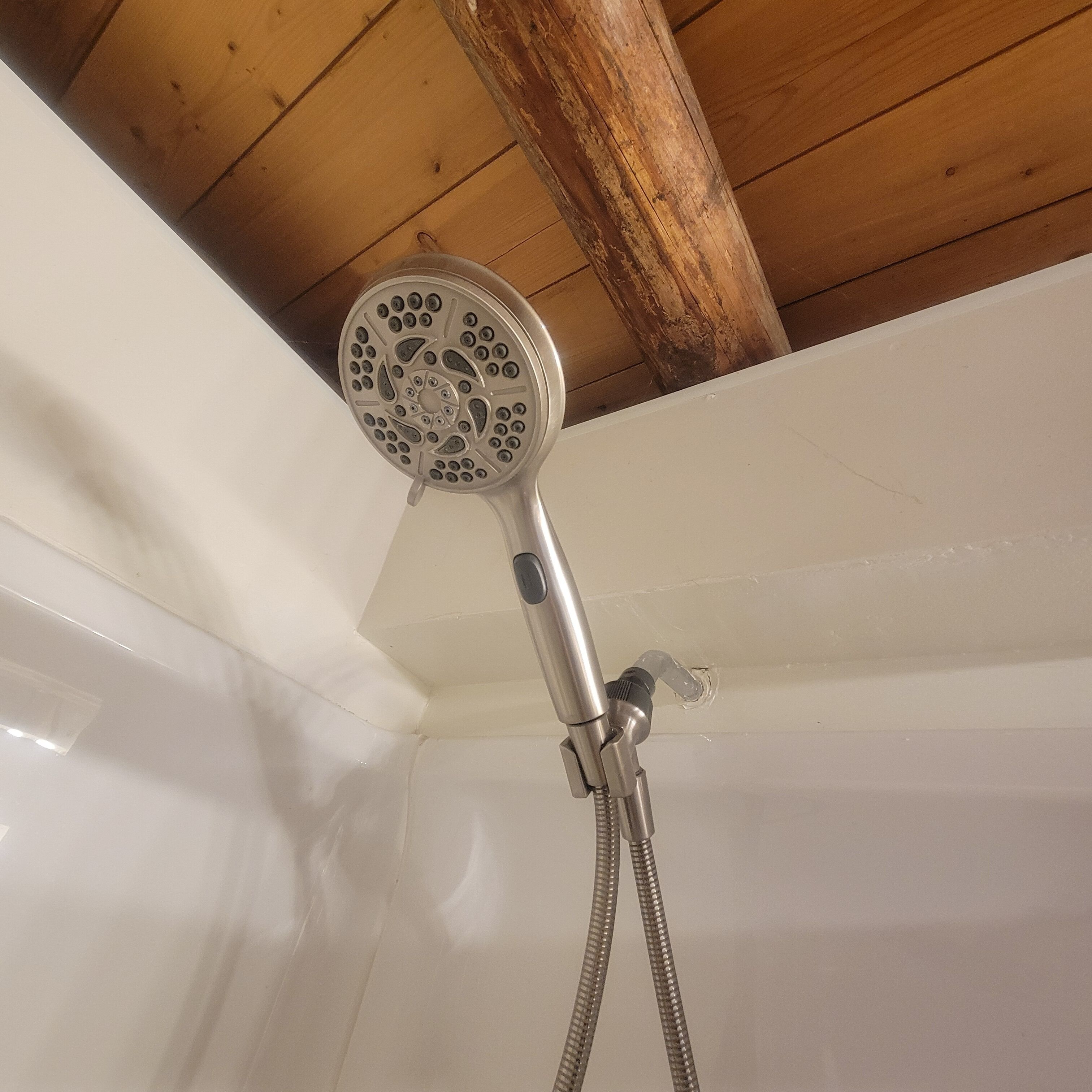 A showerhead with a flexible hose, mounted on a white wall in a room with wooden ceiling beams.