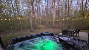 Un bain à remous éclairé d’une lumière verte, entouré d’arbres et illuminé de guirlandes lumineuses.