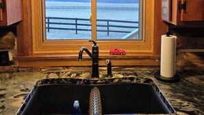 Une cuisine avec un plan de travail en bois, un évier, une fenêtre donnant sur un plan d’eau et un luminaire suspendu.