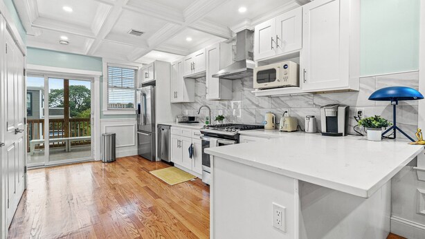 A modern kitchen with white cabinetry, a large island, stainless steel appliances, and a view to the outside.