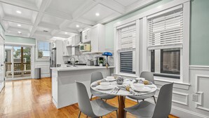 A modern kitchen with white cabinetry, a central island, and a dining area with grey chairs.