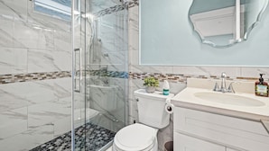 A modern bathroom with a glass shower enclosure, a toilet, and a sink with a mirror above.