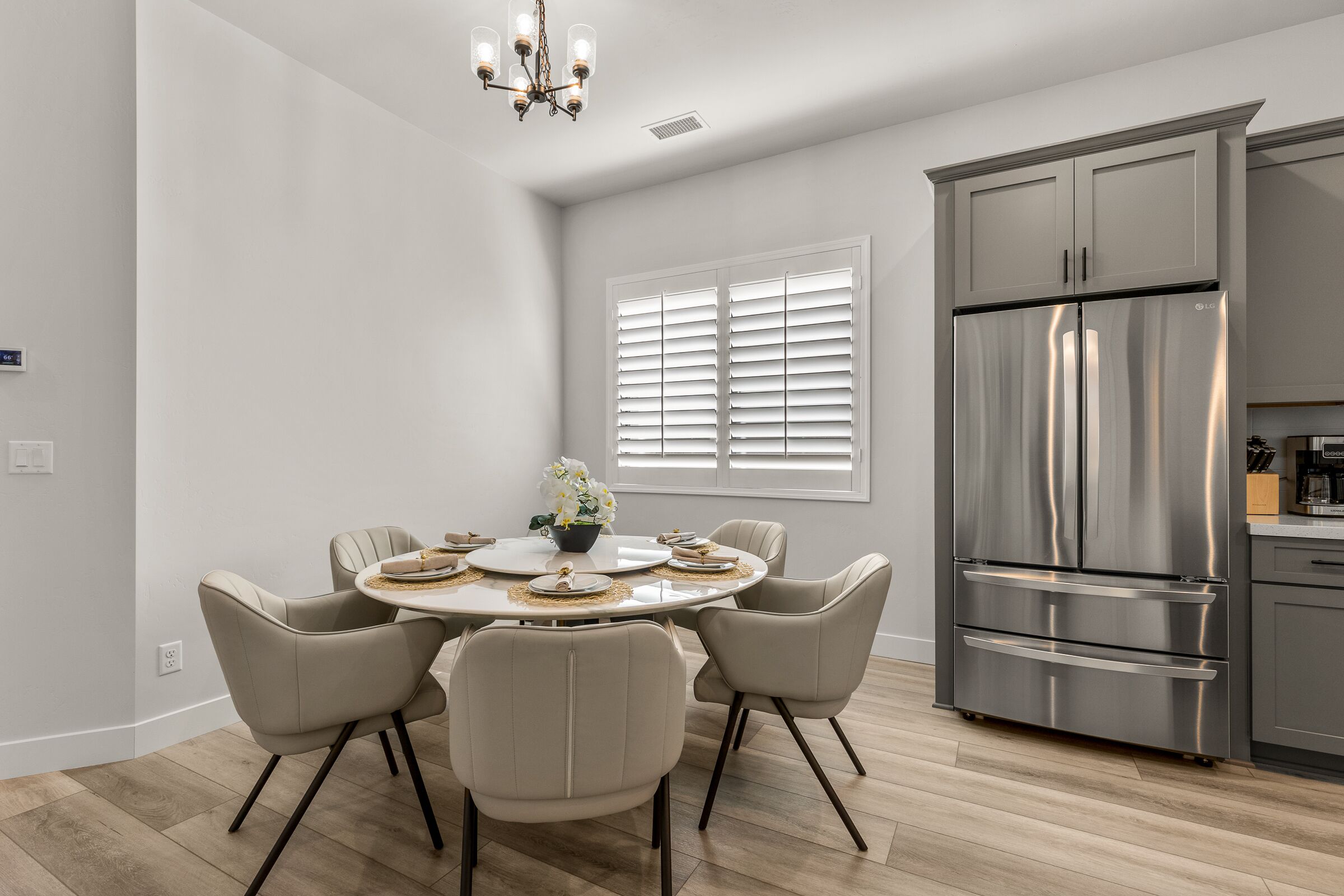 A modern kitchen with a stainless steel refrigerator, a dining area with a round table and four chairs, and a window with blinds.