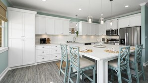 A modern kitchen with white cabinets, a central island with bar stools, stainless steel appliances, and pendant lighting.