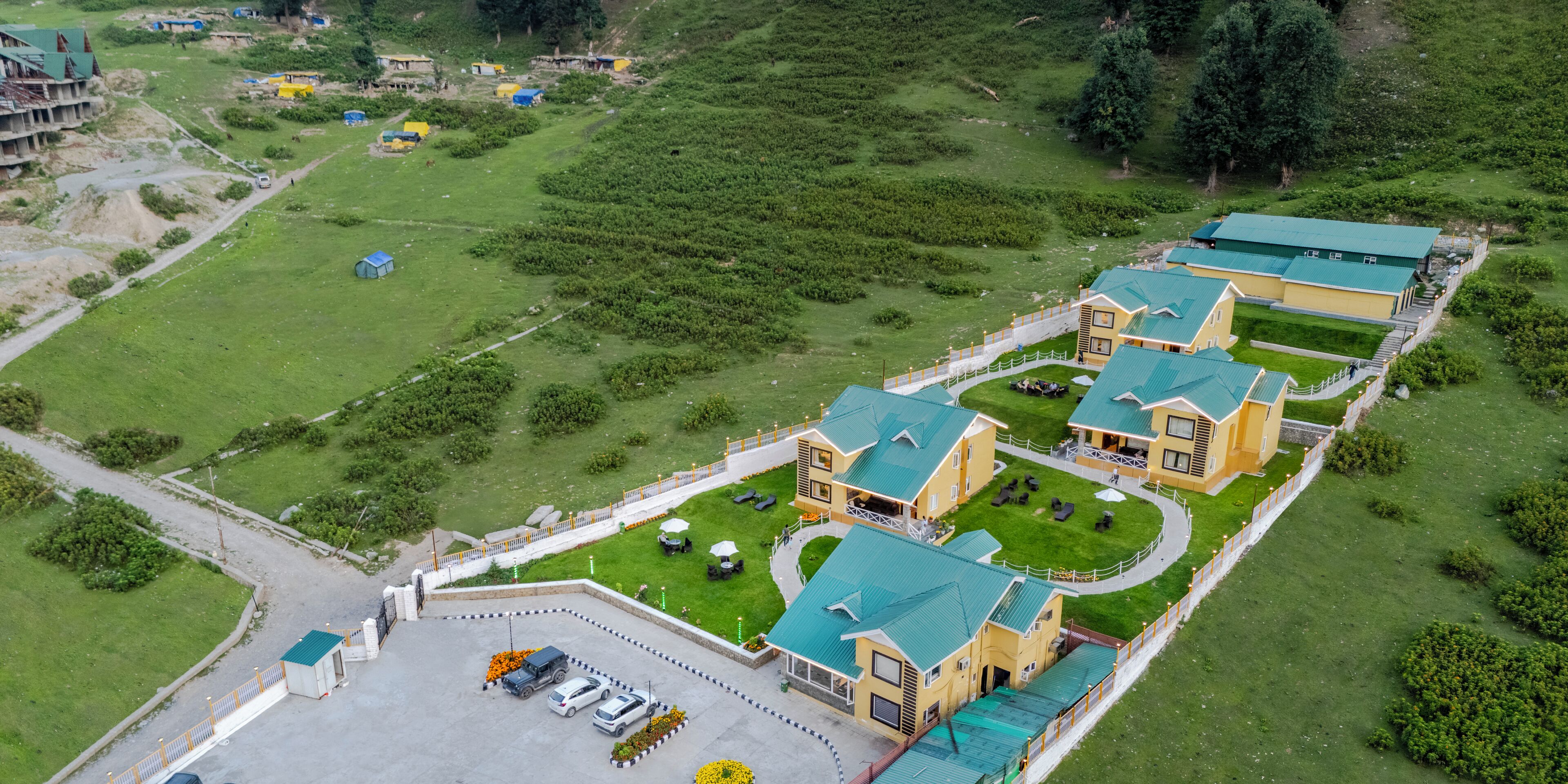 An aerial view of a hotel with multiple buildings, a parking area, and surrounding greenery.