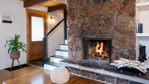 A stone fireplace with a fire, wooden stairs, and a 'Be Our Guest' sign.