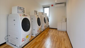 A row of four front-loading washing machines in a laundry room with wooden flooring and white walls. - HOTEL R9 The Yard Kurashiki (Kurashiki)