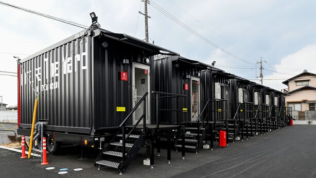 A row of black modular containers with external staircases, each with a door and a small window. - HOTEL R9 The Yard Kurashiki (Kurashiki)