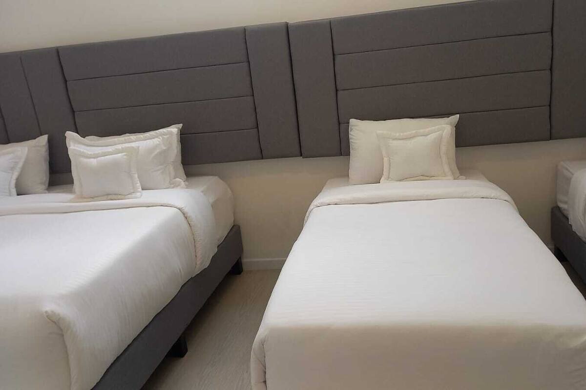 A hotel room with two single beds and a double bed, all with white bedding and grey headboards.