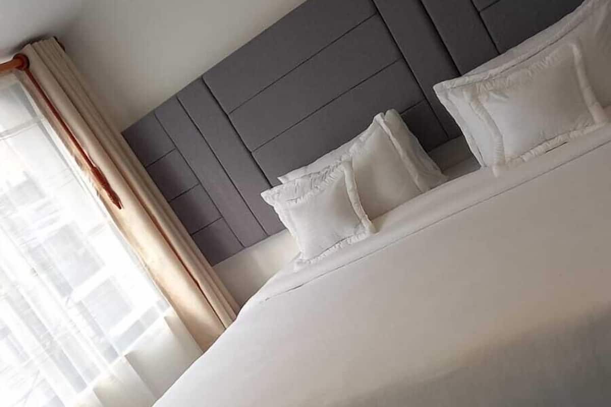 A modern hotel room with a large bed, grey headboard, and white bedding.