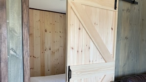 Een kamer met een wand van houten latten, een bed, een donkerbruine leren bank en een schuifdeur in boerderijstijl.