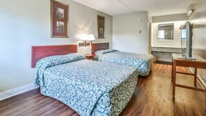 A hotel room with two beds, wooden headboard, framed pictures on the wall, a bedside table with lamps, and a wooden desk with a mirror. - Economy Hotel Macon    (Macon)