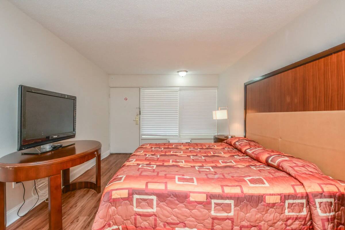 A hotel room with a bed, a television on a wooden table, and a door with a 'no entry' sign.