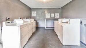 A laundry room with stacked washers and dryers, a concrete floor, and a ceiling light. - Economy Hotel Macon    (Macon)