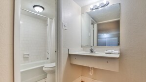A bathroom with a white bathtub, toilet, and sink with a mirror above. - Economy Hotel Macon    (Macon)