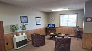 Quarto com televisão, duas cadeiras, uma mesinha e um vaso de planta.