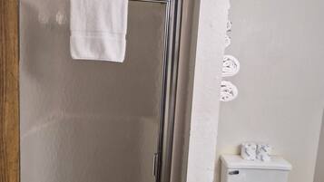 A bathroom with a glass-enclosed shower, a toilet with a black seat, and a white towel hanging on the shower door.