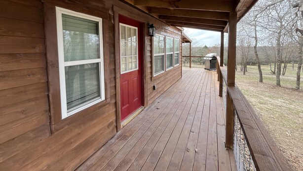 Un porche de madera con puerta roja, ventanas grandes y una parrilla en la terraza.