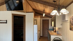 Una cocina con vigas de madera, un refrigerador, un lavamanos y un comedor con mesa y sillas.